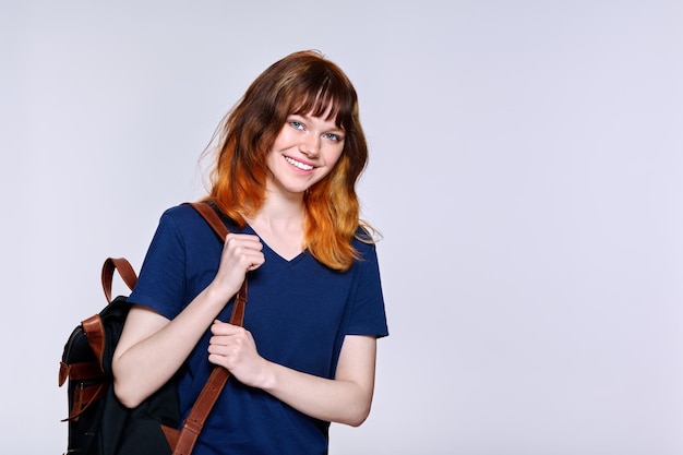 Positive redhead teenage female student with backpack looking at camera