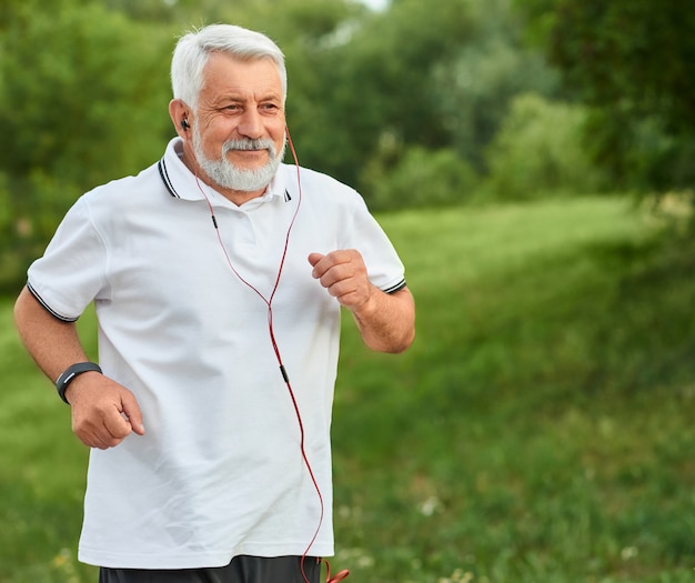 Positive running old man in green city park.