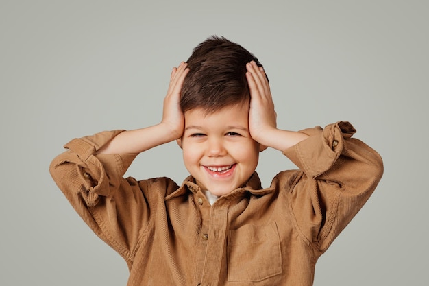 Positive shocked caucasian small child years old in shirt looks at camera holds hands on head