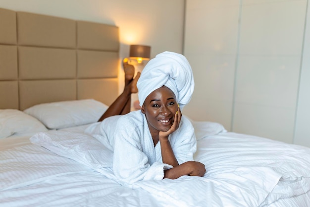 Positive start to the day Smiling african young woman lying on bed in bathrobe African american woman relaxing on the bed after bath and looking at the camera