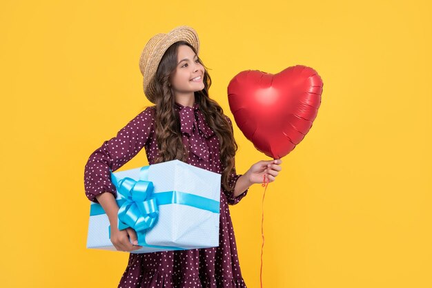 Positive teen child with red heart balloon and present box on yellow background