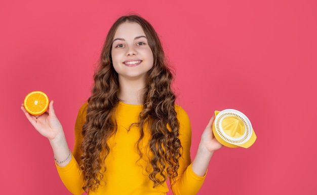 Positive teen kid hold orange and juicer on pink background