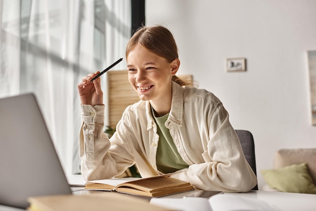 positive teenager doing homework on laptop in a home environment focus on gen z girl near books