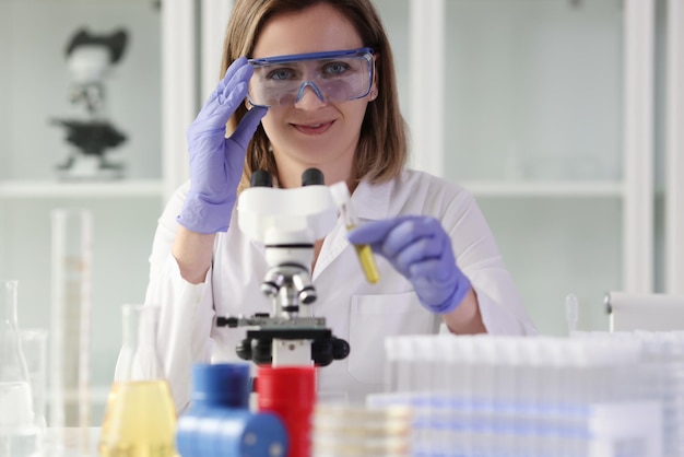 Positive woman adjusts protective goggles before examining sample under microscope looking in