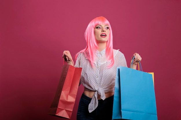 Positive woman holding shopping bags bought on sale discount, buying trendy fashionable clothes from retail store. Shopaholic person feeling joyful and having fun over pink background.