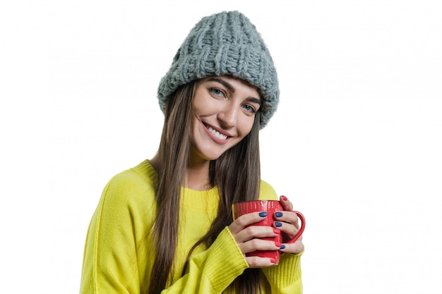 Positive woman in sweater, knitted hat with mug of hot drink