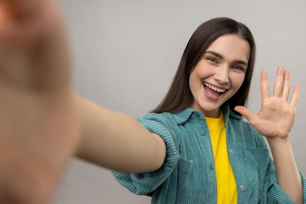 Positive woman taking selfie POV flirting expressing happiness waving hand saying hello