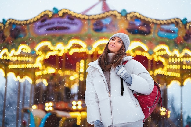 Positive woman in white coat walks at the christmas city while holds backpack lifestyle holidays