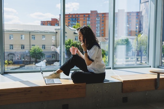 Positive woman with coffee working video call on laptop with webcams for communication happy with help woman watching comedy video on netbook in free time sitting in cafe