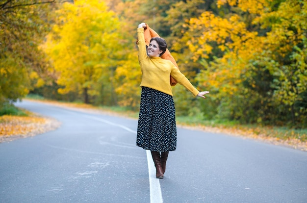 Positive woman years old in a cozy sweater looks at the camera along the road in the autumn forest o