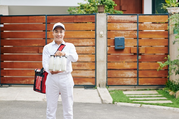 Positive young Asian delivery man in white unifrom holding wire milk crate with