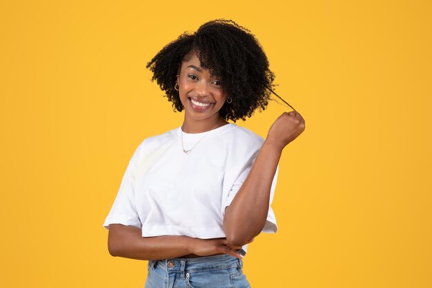 Positive young black curly woman in white tshirt touches hair flirts