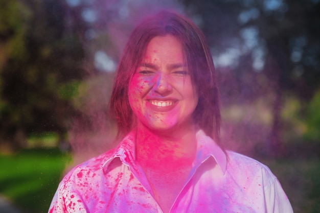 Positive young caucasian woman playing with pink dry paint at the Holi Festival in the park