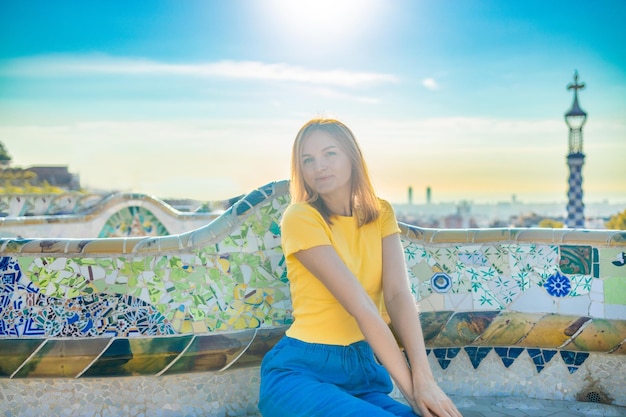 Positive young female tourist sitting on stone bench and checking photos while resting during vacation at Park Guell