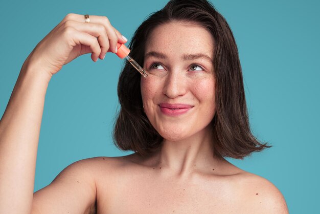 Photo positive young lady applying oil serum on face in blue studio