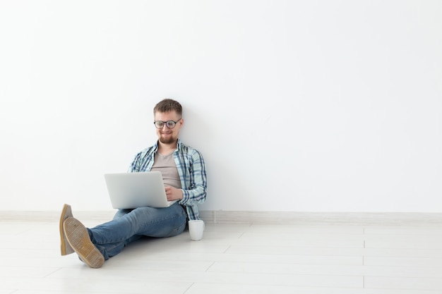 Positive young man in casual clothes and glasses surfing the Internet using Wi-Fi and a laptop in search of rental housing. Housewarming and apartment search concept, copy space