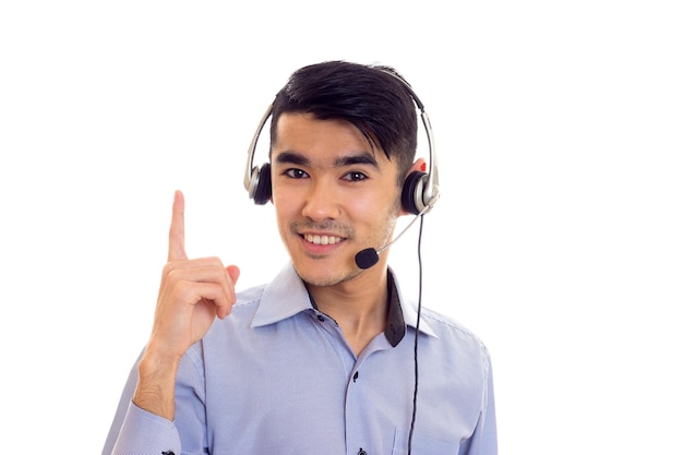 Positive young man with dark hair in blue shirt with black headphones on white background in studio