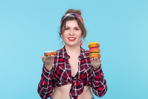 Positive young pin-up girl model holding in hands multicolored doughnuts