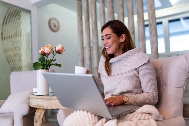 Positive young woman freelancer watching video in blog on netbook and having a coffee at comfortable home. Beautiful young business woman working on laptop.Freelancer connecting to internet