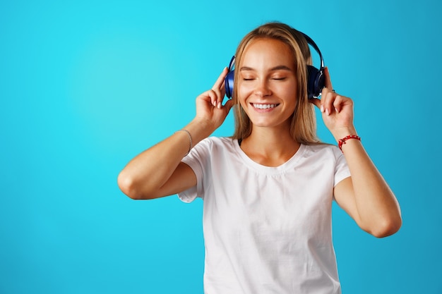 Positive young woman listening to music with blue headphones close up