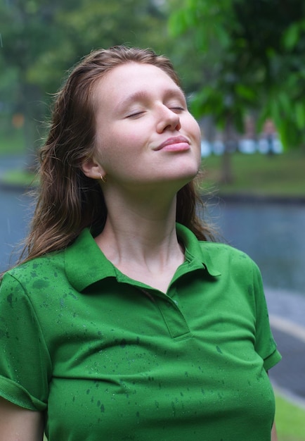 Positive young woman smiling during the rain in the park cheerful female enjoying the rain outdoors