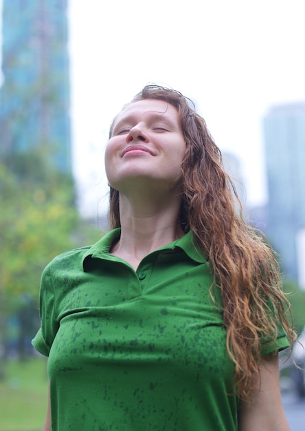 Positive young woman smiling during the rain in the park cheerful female enjoying the rain outdoors