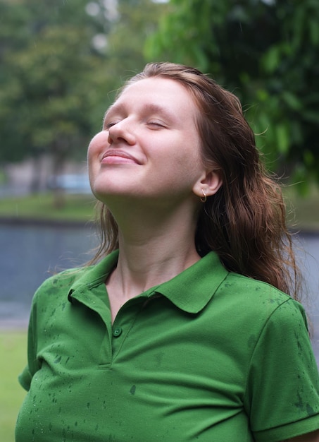 Positive young woman smiling during the rain in the park cheerful female enjoying the rain outdoors