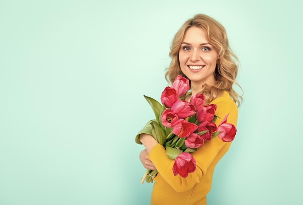 Positive young woman with spring tulip flowers on blue background