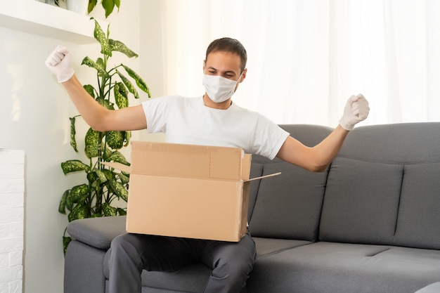 post, home and lifestyle concept - man with boxes in mask and gloves on sofa