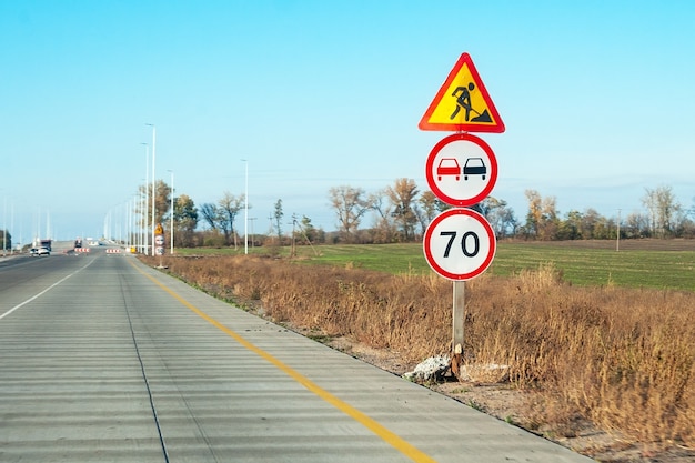 Post with warning road signs: road construction works, no passing and speed limit of 70 km/h