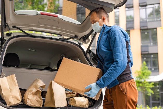 Postal delivery courier man wearing protective face mask in front of cargo van delivering package holding box due to Coronavirus disease or COVID-19.