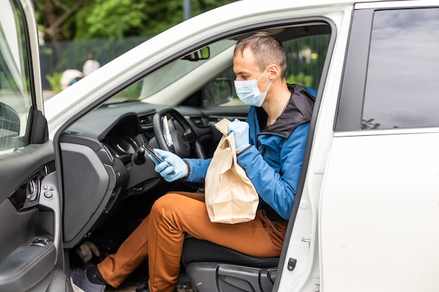 Postal delivery courier man wearing protective face mask in front of cargo van delivering package holding box due to Coronavirus disease or COVID-19.