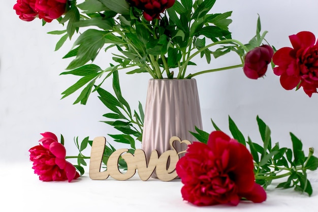 Postcard with a bouquet of scarlet peonies and a wooden inscription love on a white background