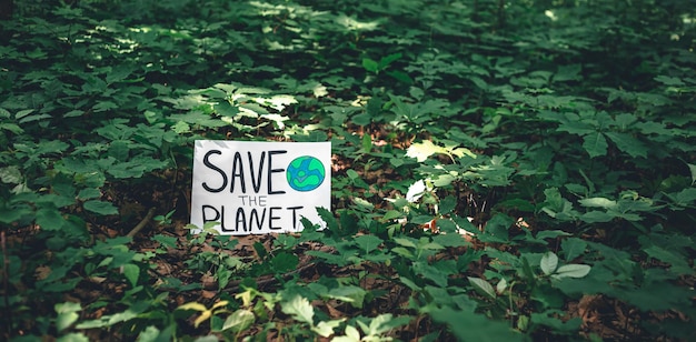 Poster with the inscription save the planet in the forest among the plants