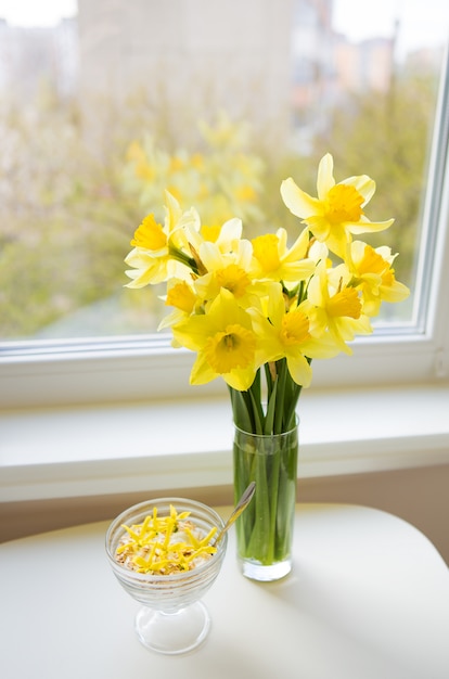 Posy of bright yellow daffodils on white wooden table.