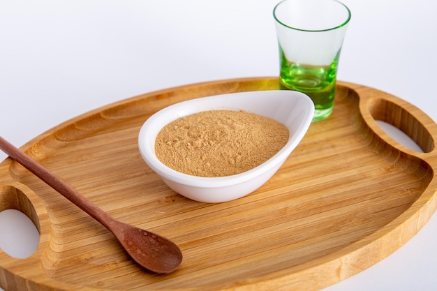 Pot of Peruvian Maca powder under a bamboo tray selective focus on white background