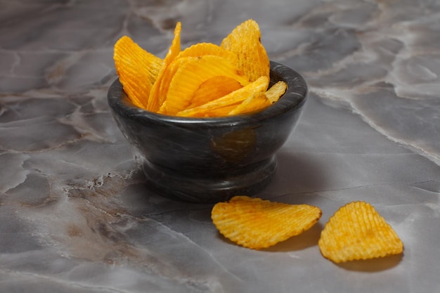 Potato chips in a black stone bowl. Top view.