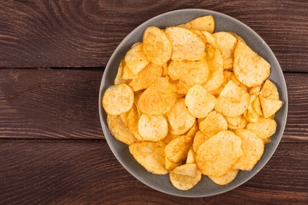 Potato chips in bowl on wooden background top view