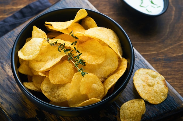 Potato chips Fast food Crispy potato chips ceramic black bowl with sour cream sauce and onions in wooden stand on old kitchen table wooden background American tradition Hot BBQ Top view