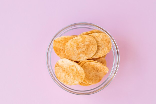 Potato chips in glass bowl on pink background Fast food