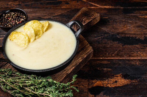 Photo potato cream soup with potato chips in pan on wooden board