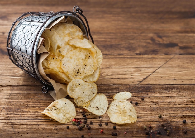 Potato crisps chips with black pepper in steel snack bucket on wooden table background Best snack for beer and soda drinks