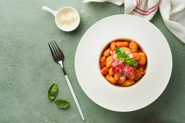 Potato gnocchi Traditional homemade potato gnocchi with tomato sauce basil and parmesan cheese on kitchen table on light green kitchen table background Traditional Italian food Top view