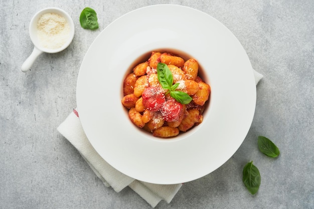 Potato gnocchi Traditional homemade potato gnocchi with tomato sauce basil and parmesan cheese on kitchen table on light grey kitchen table background Traditional Italian food Top view