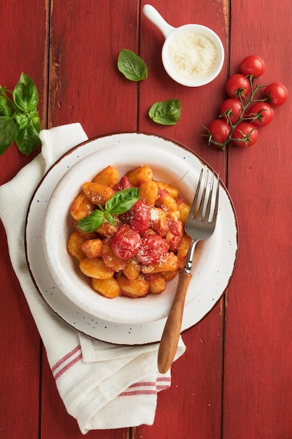 Potato gnocchi Traditional homemade potato gnocchi with tomato sauce basil and parmesan cheese on red rustic kitchen table background Traditional Italian food Top view