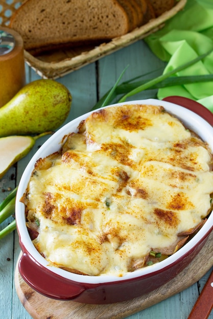 Potato gratin with pear raclette cheese and bacon on rustic wooden table