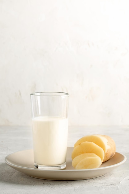 Potato milk in glass with cut potato purified tuber on beige plate on light backdrop Copy space