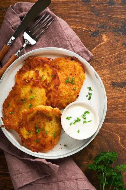 Potato pancakes Fried homemade potato pancakes or latkes with cream and green onions in rustic plate on old wooden brawn table background Rustic style Healthy food Top view