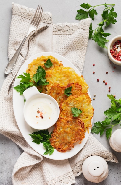 Potato pancakes with sour cream, herbs and garlic in white ceramic plate on gray old concrete table.