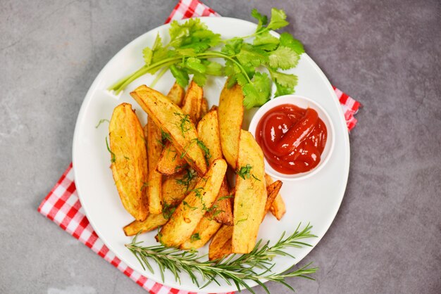 Potato wedges on white plate with rosemary herb coriander and tomato ketchup sauce Cooking french fries or fry potatoes